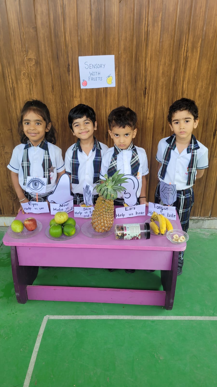 Four children in uniform beside a table of fruit labelled with the five senses