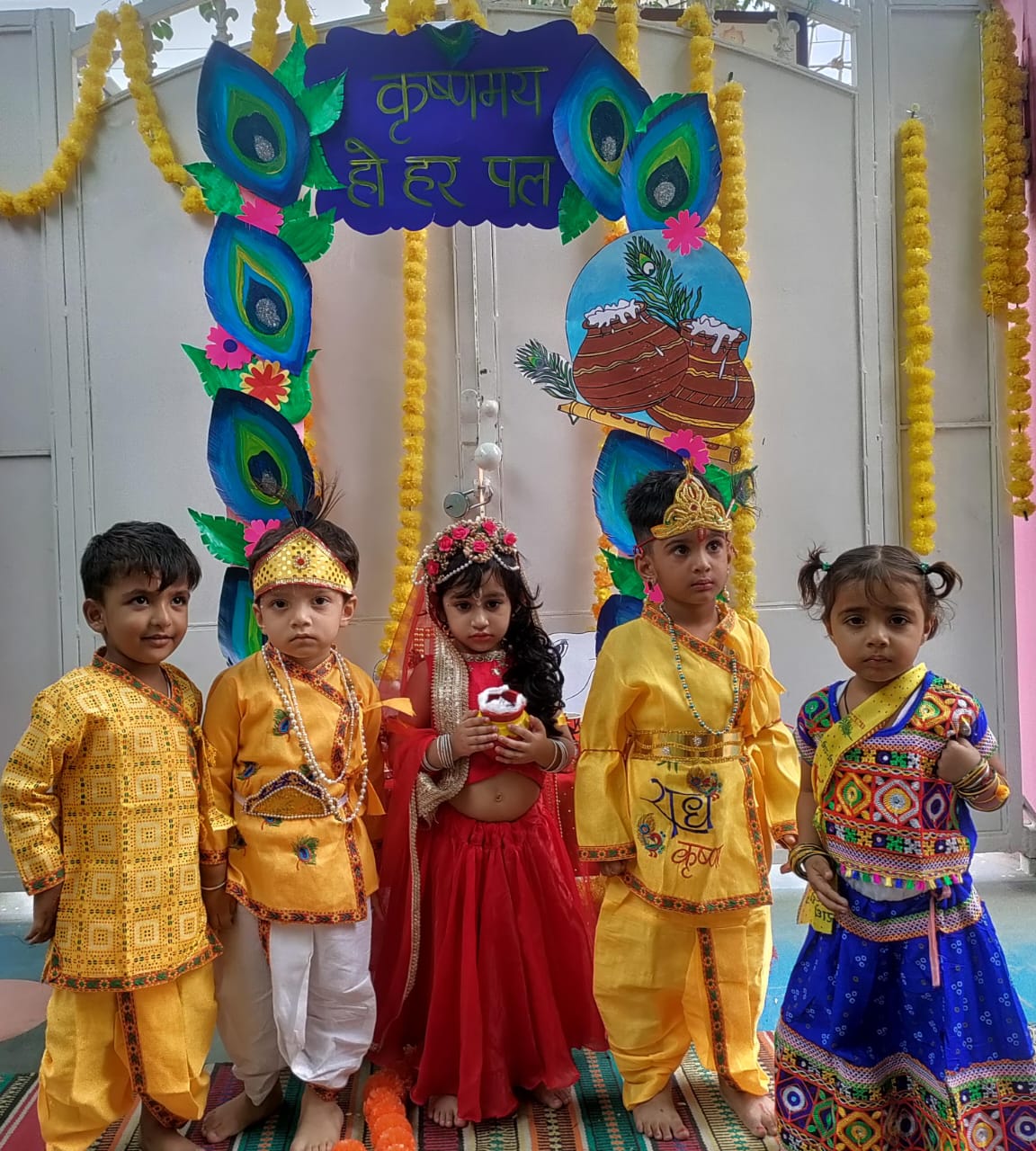 Children dressed as Radha and Krishna in front of a festival arch