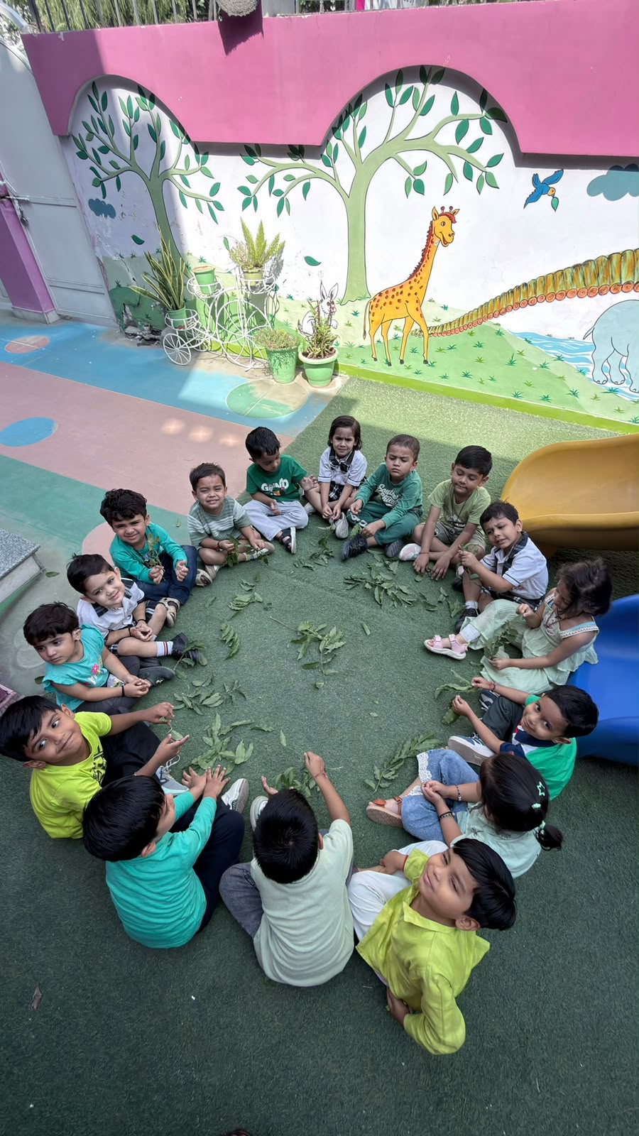 Children sitting in a circle of leaves in front of the giraffe mural