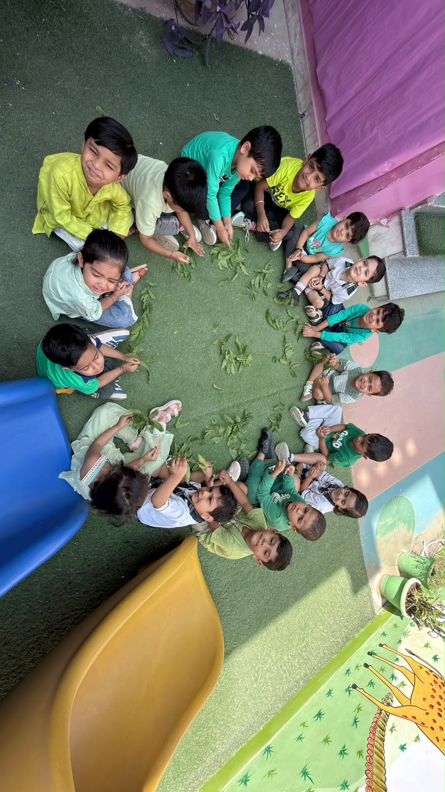 Children sitting in a circle sorting leaves beside the slides