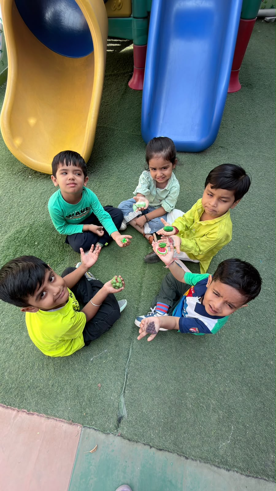 Children sitting on the play area grass in front of the slides