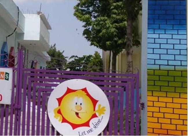 The smiling sun mascot painted on the Sirsi Road gate